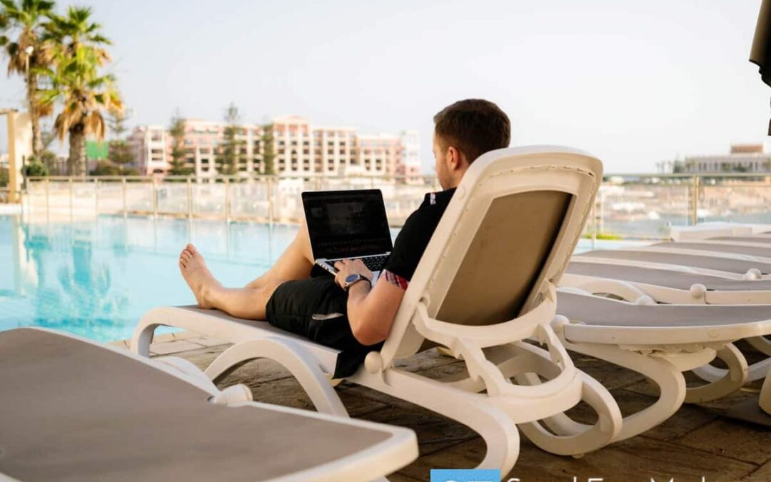 A person sitting on a lounge chair next to a pool working on a computer.