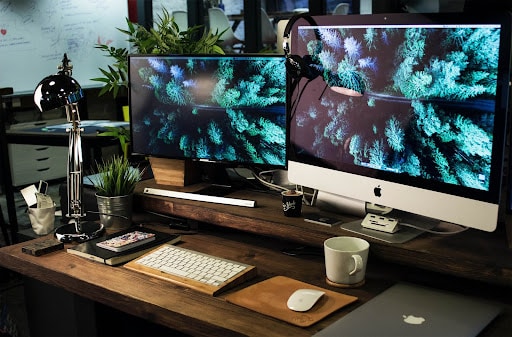 A wooden work with two computer screens displaying a nature background.