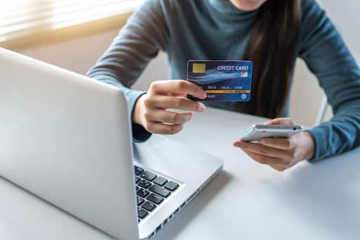 A person readying their credit card to make an online purchase on their laptop.
