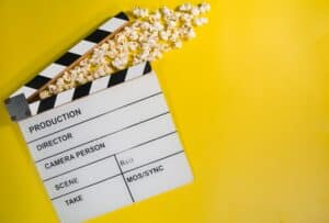 A clapperboard with popcorn coming out of the moving arm on a yellow background.